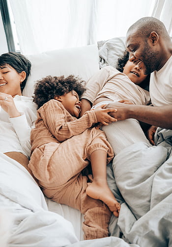 A joyful family shares a playful moment in bed, embodying love and togetherness. HD phone wallpaper
