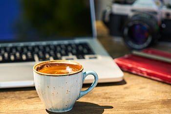 A cozy workspace with a cappuccino, laptop, and vintage camera on a wooden desk. HD wallpaper