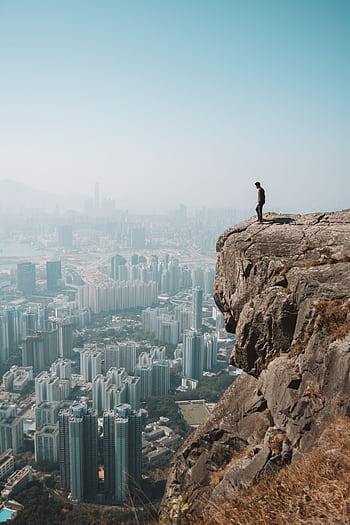 Man stands on cliff overlooking stunning Hong Kong skyline, capturing the blend of urban and natural environments. HD phone wallpaper