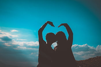 Silhouette of a couple creating a heart shape with their arms in a romantic outdoor setting. HD wallpaper