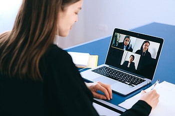 A woman engaging in a video conference using a laptop at home, taking notes. HD wallpaper