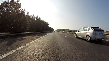 White car traveling on a clear highway in Hatfield, England with scenic trees. HD wallpaper