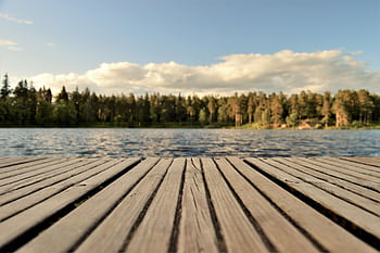 Serene wooden dock with a forested lake view under a bright summer sky in Sweden. HD wallpaper