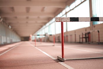 Empty indoor athletic track featuring hurdles for training sessions. HD wallpaper