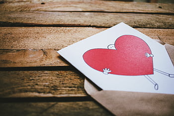A charming heart illustration on a card inside an envelope placed on a rustic wooden table, perfect for Valentine's Day. HD wallpaper