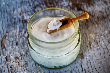 Close-up of organic coconut oil in glass jar with wooden spoon, perfect for natural health and wellness use. HD wallpaper