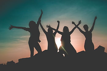 Four women enjoying a fun silhouette moment during a vibrant Kenyan sunset. HD wallpaper