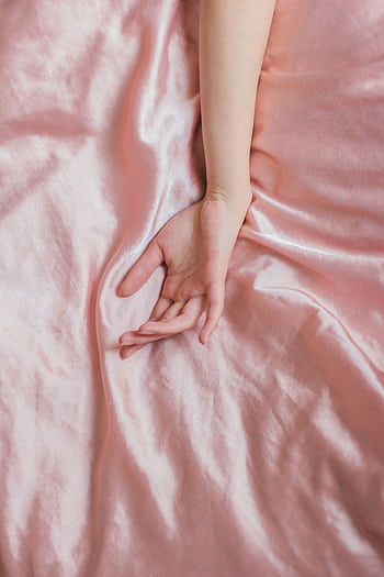 A close-up of a female hand resting gently on an elegant pink silk sheet, evoking serenity and comfort. HD phone wallpaper