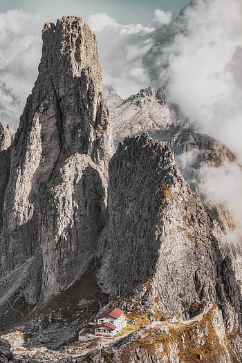 Breathtaking view of the Dolomites with rugged peaks and an alpine hut nestled below, enveloped by clouds. HD phone wallpaper