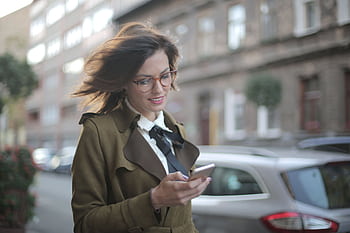 A young woman with glasses smiling as she uses her smart outdoors. HD wallpaper