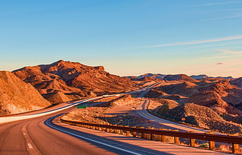 Stunning view of a winding highway amidst Nevada's rugged landscape under blue skies at sunset. HD wallpaper