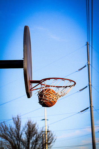 A basketball perfectly swishes through the hoop on an outdoor court against a clear blue sky. HD phone wallpaper