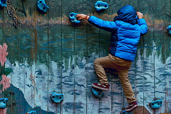 Young boy in blue jacket climbing a painted rock wall outdoors, showcasing adventure and play. HD wallpaper
