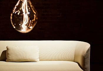 A contemporary interior featuring a glowing light bulb and a stylish beige sofa against a dark backdrop. HD wallpaper
