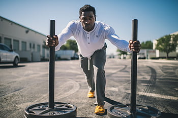 Man in athletic wear pushing sled outdoors, showcasing strength and determination. HD wallpaper