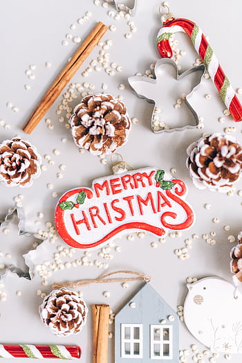 A flat lay of Merry Christmas decorations with pine cones, candy cane, and cookie cutters on a winter theme background. HD phone wallpaper