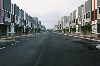 A quiet, empty urban street flanked by modern condominiums under a cloudy sky, with ample parking space. HD wallpaper