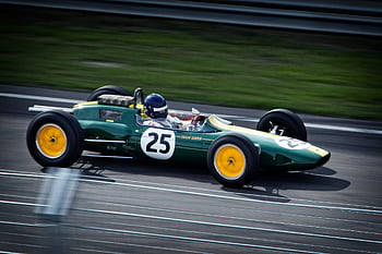 A green vintage Formula 1 car with number 25 speeds around a racetrack, showcasing classic racing heritage. HD wallpaper