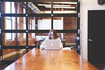 A young woman works on a laptop in a modern, industrial-style office with exposed brick walls. HD wallpaper