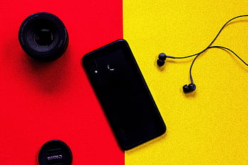 Colorful flat lay featuring a smart, camera lens, and ears on a red and yellow background. HD wallpaper