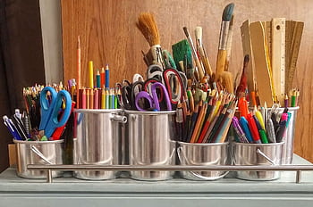 A diverse collection of art supplies in metallic buckets on a wooden table. HD wallpaper