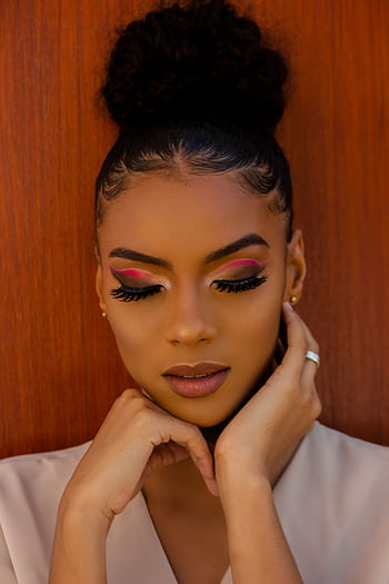 Close-up portrait of a woman with elegant hairstyle and vibrant eye makeup against a wooden background. HD phone wallpaper