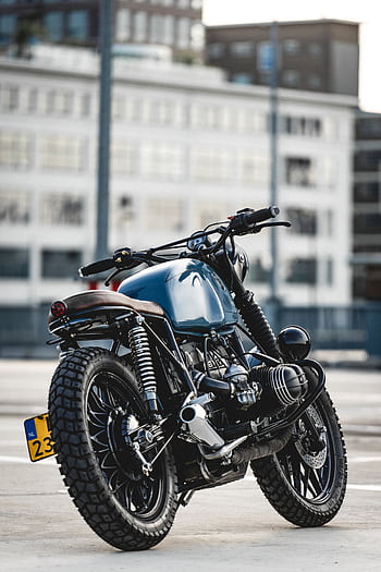 A sleek cafe racer motorcycle parked on asphalt with modern architecture in the background. HD phone wallpaper