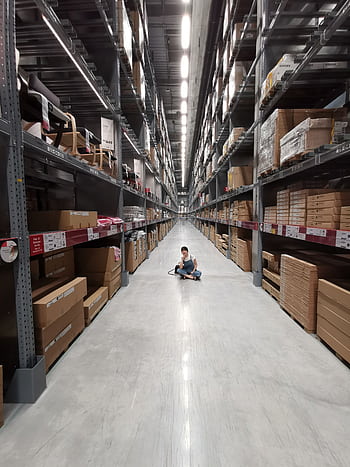 An Asian woman sits in a large warehouse aisle filled with inventory racks and shelves. HD phone wallpaper