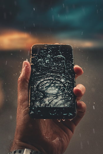 A person holds a smart with raindrops on screen, emphasizing water resistance. HD phone wallpaper