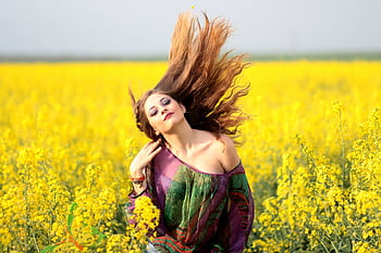 Vibrant portrait of a woman in a yellow flower field, exuding happiness and dom. HD wallpaper