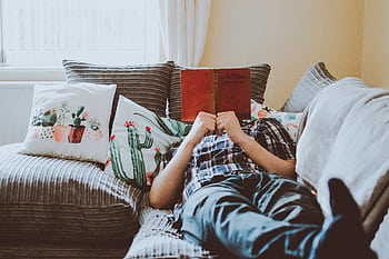 Relaxing at home, lying on a sofa with a book and cushions around. HD wallpaper