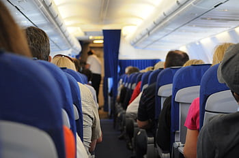 Interior view of an airplane cabin with passengers seated, showcasing air travel experience. HD wallpaper