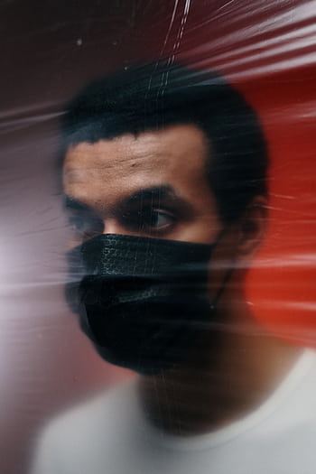 Portrait of a man wearing a mask behind a blurred surface, depicting isolation and protection. HD phone wallpaper