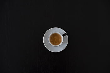 Flat lay of a white coffee cup with espresso on a black table, highlighting minimalist design. HD wallpaper