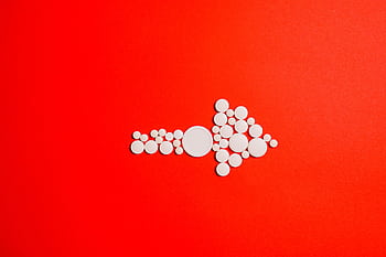 White pills form an arrow shape on a bold red backdrop, symbolizing direction in healthcare. HD wallpaper