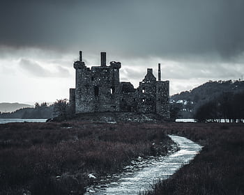 A historic Scottish castle sits by a lake under a dark, stormy sky, creating a moody atmosphere. HD wallpaper