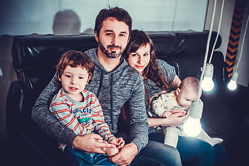 A joyful family of four sitting on a sofa, smiling warmly indoors. HD wallpaper