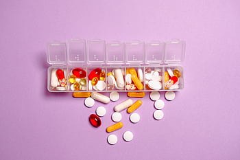A daily pill organizer filled with various pills and capsules on a purple background. Ideal for healthcare topics. HD wallpaper