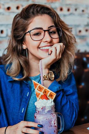 A smiling woman in glasses enjoying a colorful beverage indoors, featuring waffles and whipped cream. HD phone wallpaper