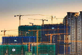 A cityscape featuring high-rise buildings under construction with cranes during sunset. HD wallpaper