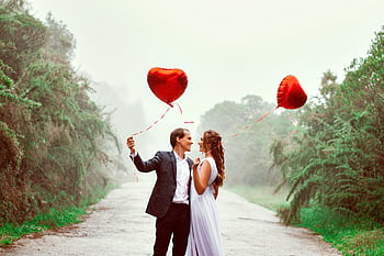 A loving couple embraces with heart-shaped balloons in a foggy park setting. HD wallpaper