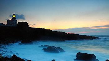 lighthouse on a rocky shore shining a green light, sea, shore, lighthouse, light, dusk, rocks HD wallpaper