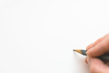 Close-up of a hand sketching on white paper with a pencil, emphasizing creativity. HD wallpaper