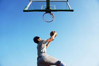 A young man jumping to dunk a basketball outdoors in clear daylight. HD wallpaper