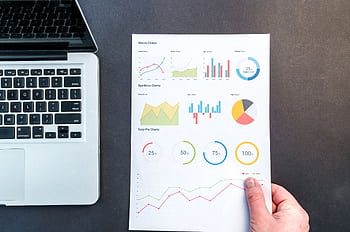 Detailed charts and graphs on a document next to a laptop, representing data analysis. HD wallpaper