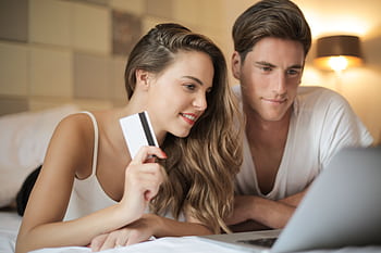 Smiling couple using credit card for online shopping on laptop at home. HD wallpaper