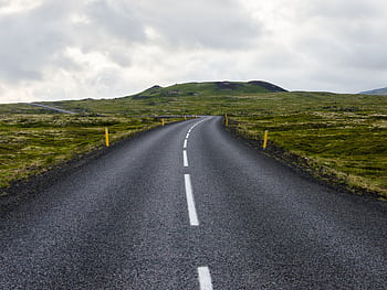 Empty road stretches through lush countryside under cloudy skies, ideal for travel themes. HD wallpaper