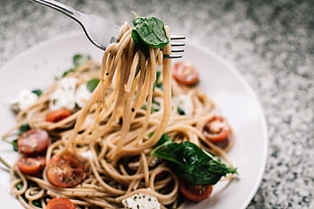 Delicious whole wheat pasta with fresh spinach, cherry tomatoes, and feta cheese in a close-up shot. HD wallpaper