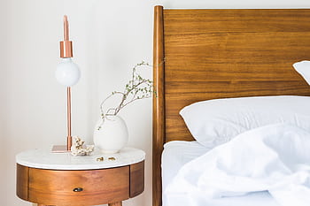 A modern bedroom setup featuring a wooden bed, stylish lamp, and round side table with a plant. HD wallpaper
