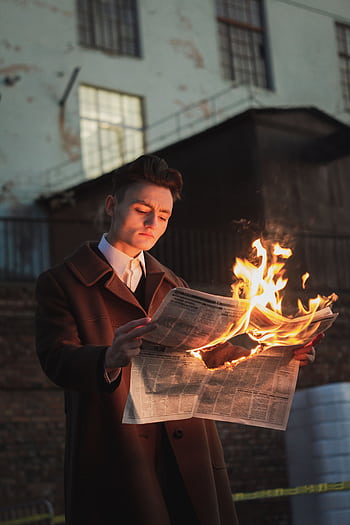 A man in a coat reads a burning newspaper outside at night, dramatic scene. HD phone wallpaper